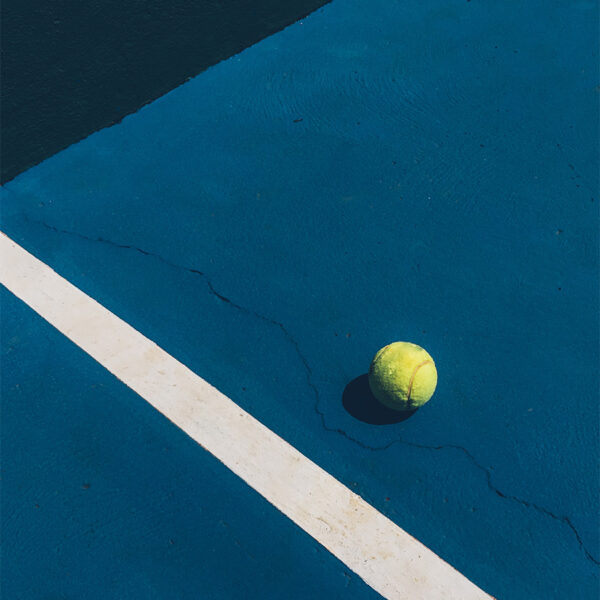 Detail of tennis ball on dark blue tennis court with bright white diagonal stripe.