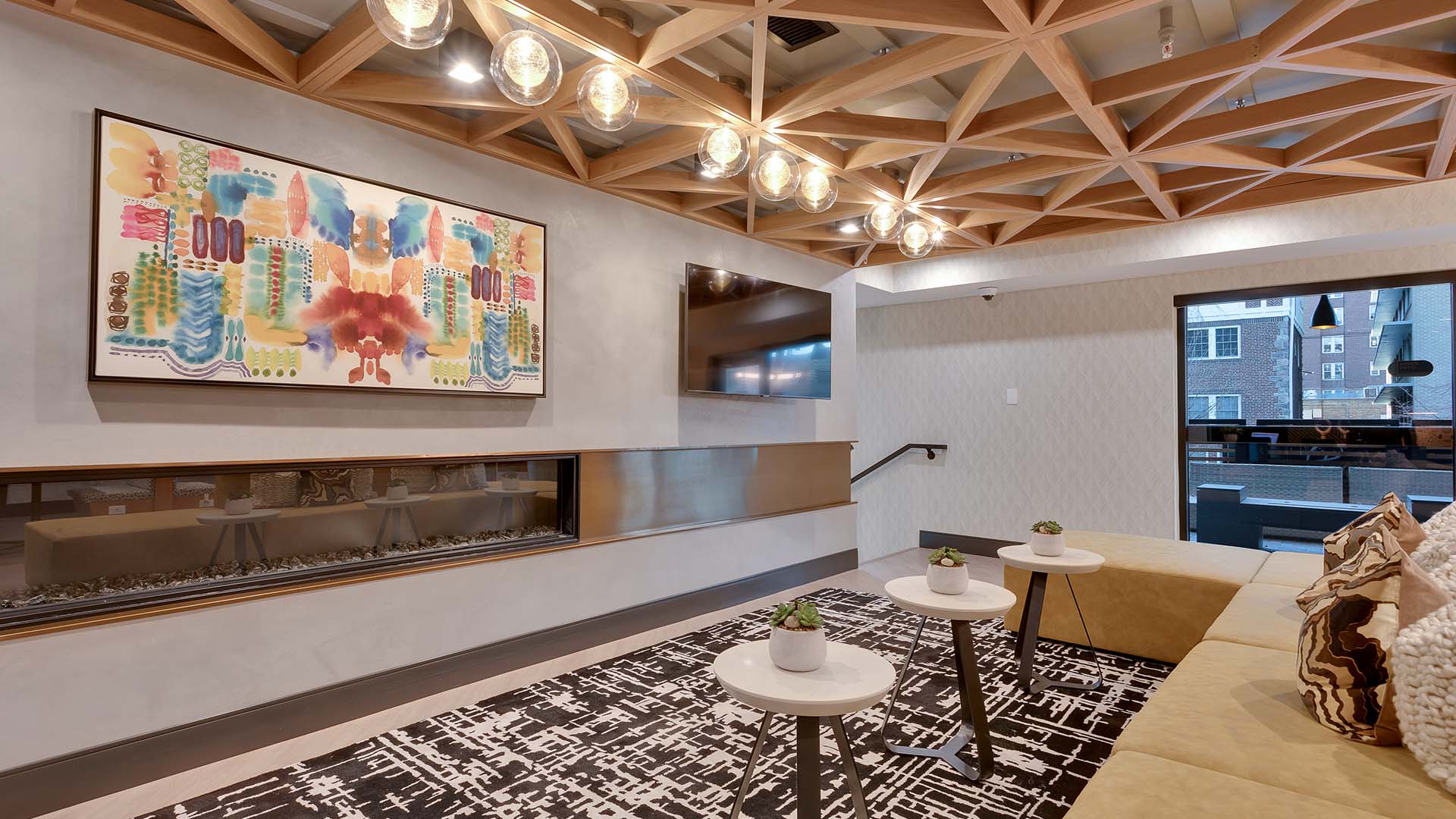 Lounge with pattern carpet, plush sectional with pillows, large fireplace, and wall mounted TV.