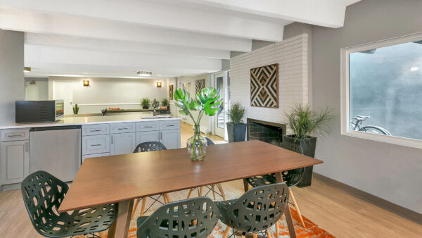 Community kitchen with island, wood table with modern chairs, large window, and brick accent wall with fireplace.