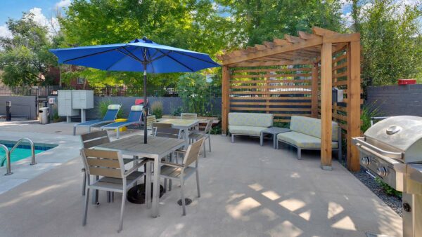 Pool area with lounge chairs, tables, umbrellas, and wood pergola.