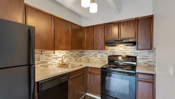 Kitchen with wood floor and cabinets, light counters, black appliances, and tiled backsplash.