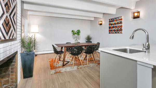 Lounge with wood floor, modern dining table, brick accent wall with fireplace, and wall art.