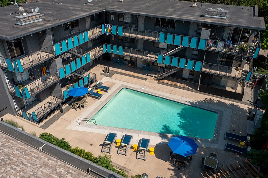 Aerial view of 833 Dexter with bright blue pool, lounge chairs, umbrellas, and apartment balconies.