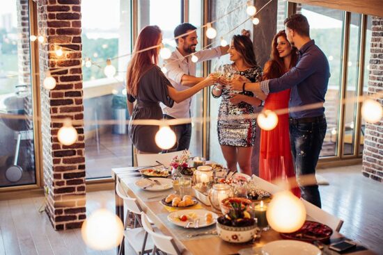 Friends drinking wine at party with string lights and table with foods and candles.
