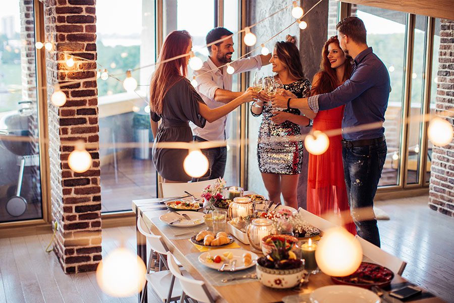 Friends drinking wine at party with string lights and table with foods and candles.