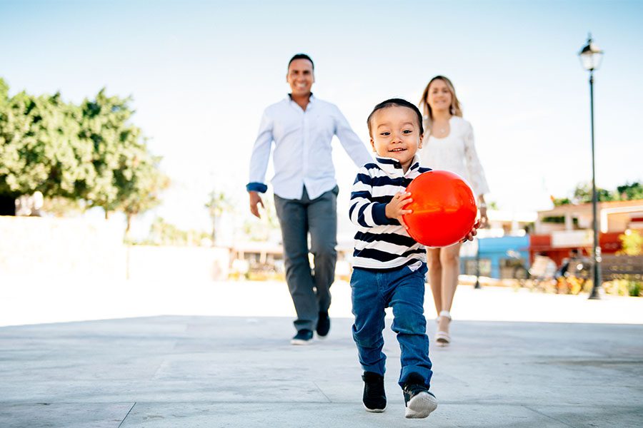 Family walking outside with child carrying ball.