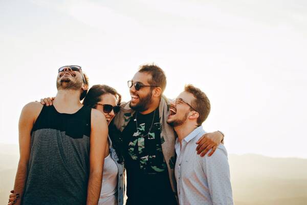 Friends laughing outside with arms around each other.