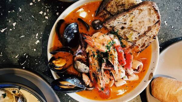 Plates of Italian dishes with shellfish and bread on stone table.