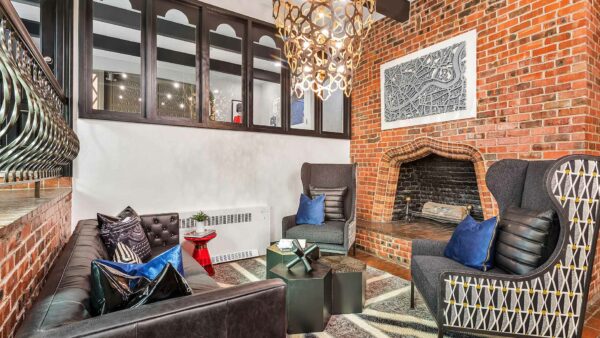Lounge with brick fireplace, rug, classic wingback chairs, leather couch, and chandelier.