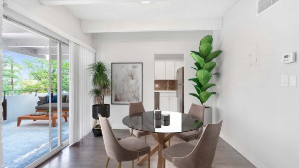 Dining room with glass table, plush chairs, large potted plants, and doors to kitchen and balcony.