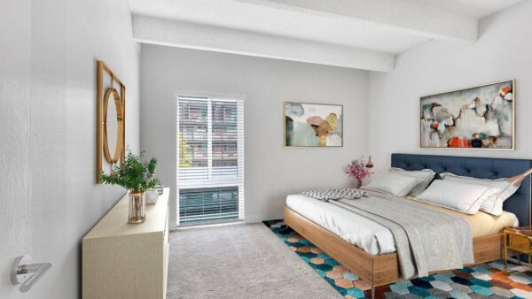 Bedroom with carpet, geometric rug, bed with plush headboard, artwork, and large window.