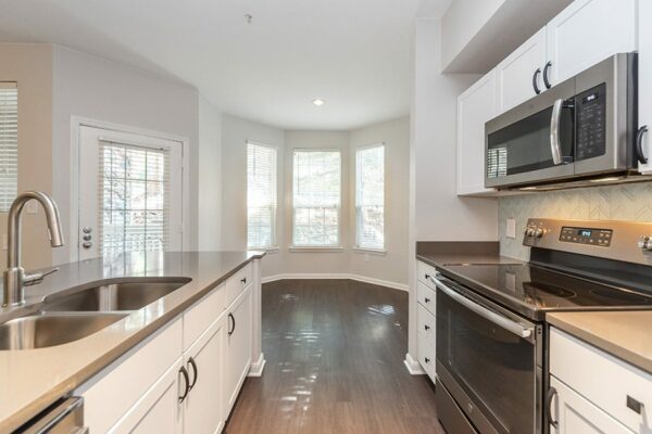Kitchen with wood floor, white cabinets, grey counters, stainless steel appliances, and bright dining area.