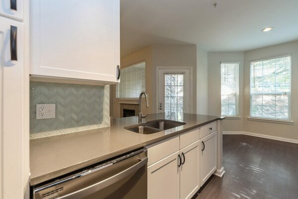 Kitchen with wood floor, white cabinets, grey counters, tiled backsplash, and bright dining area.