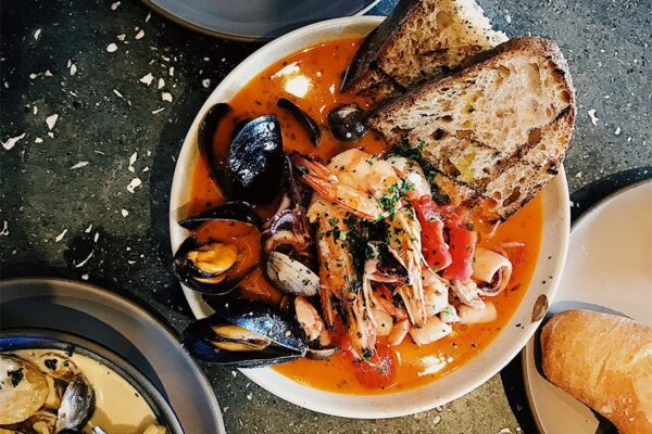 Plates of Italian dishes with shellfish and bread on stone table.
