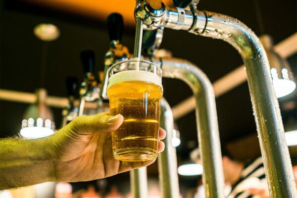 Person pouring light golden beer into glass from metal tap.