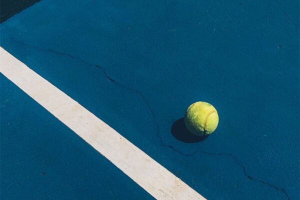 Detail of tennis ball on dark blue tennis court with bright white diagonal stripe.