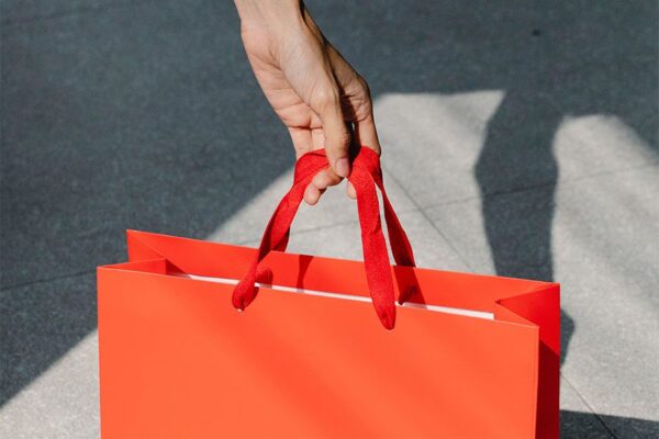 Person holding bright red shopping bag on concrete sidewalk.