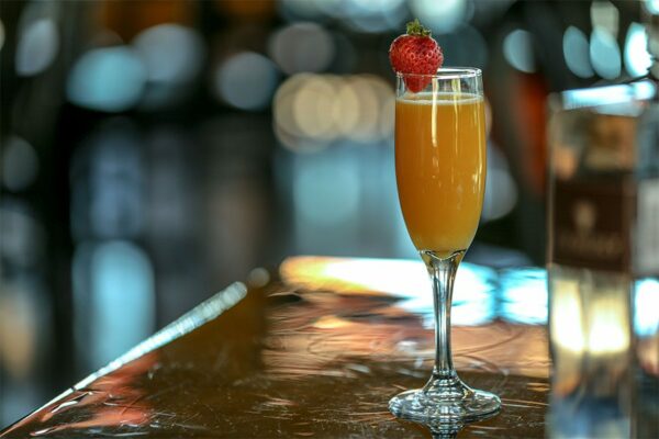 Mimosa in champagne flute with strawberry on table with out of focus lights behind.