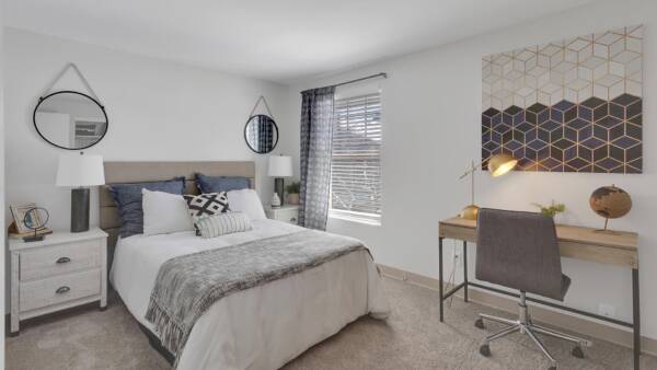 Guest bedroom with carpet, large bed, large closet, desk with lamp, and large artwork.