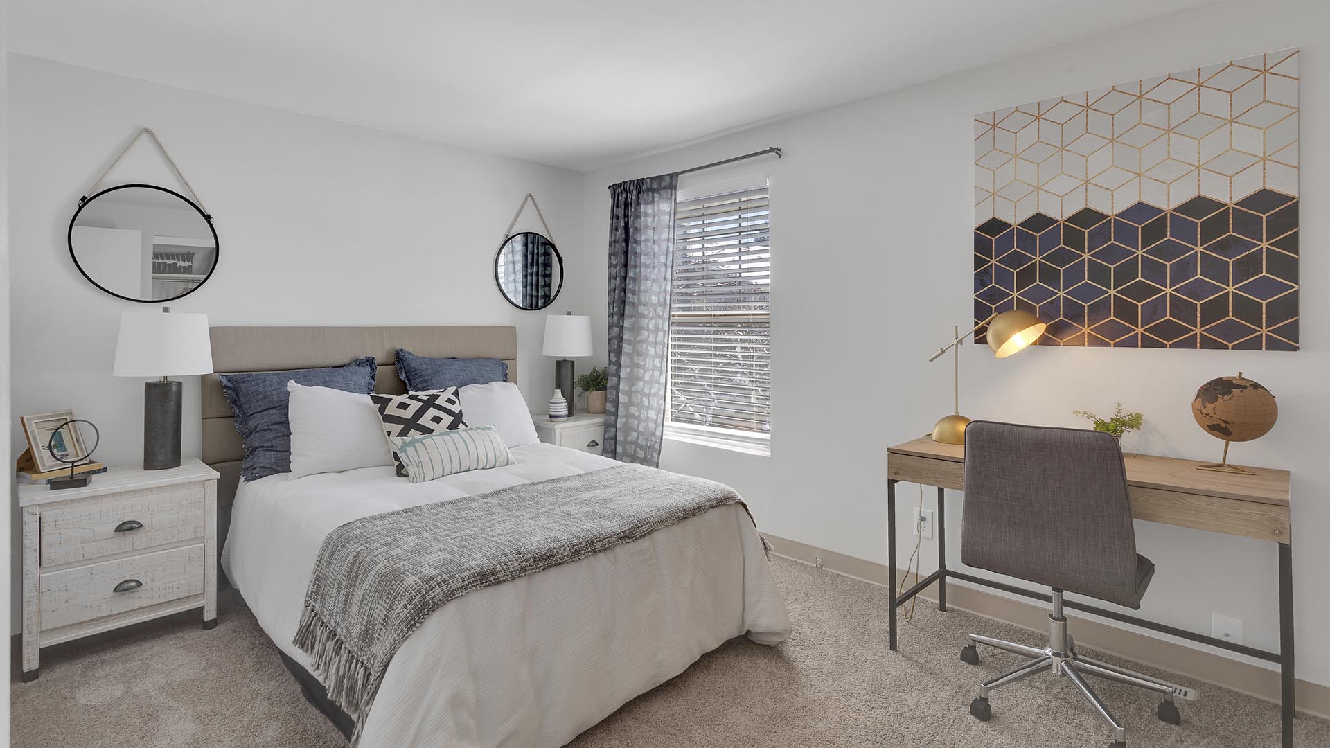 Guest bedroom with carpet, large bed, large closet, desk with lamp, and large artwork.