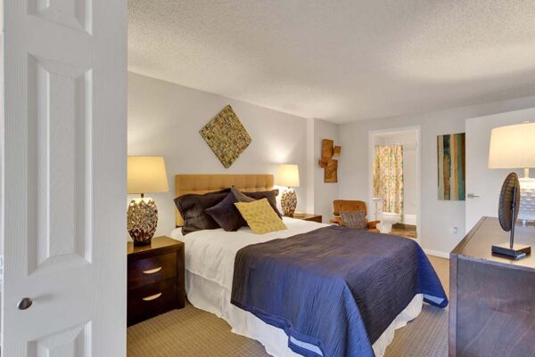 Furnished bedroom with white walls, tan carpet, and artwork on the walls.