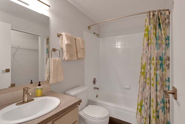 Bathroom with tan cabinets, a full bathtub with white tiles, and a dark tan countertops.