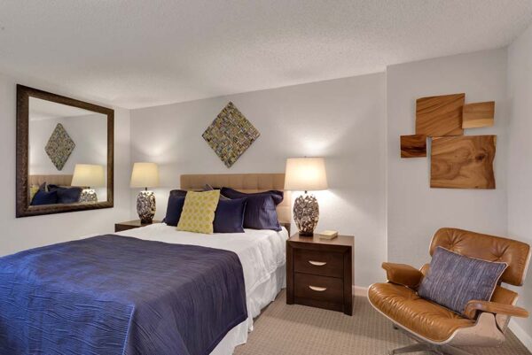 Furnished bedroom with white walls, tan carpet, and artwork on the walls.