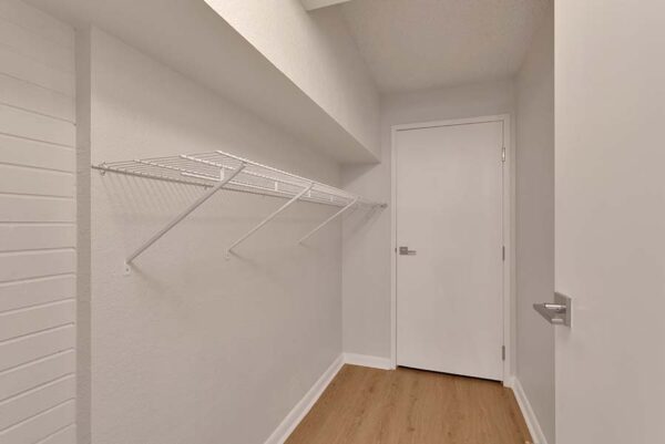 A large closet with white walls, wood floors, and shelving.