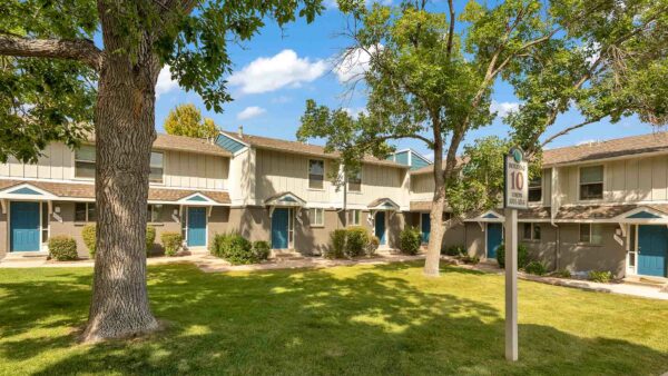 Exterior view of apartments by grass and trees with a tan exterior.