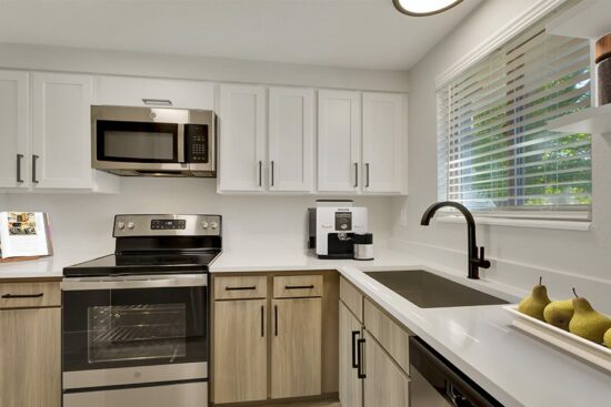 Kitchen with white countertops, stainless steel appliances, white overhead cabinets, and tan lower cabinets.