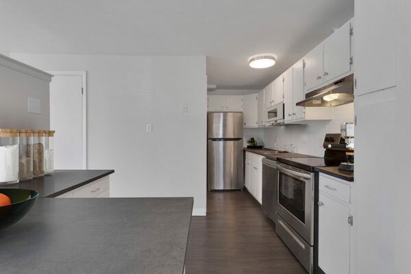 Rendering of a furnished kitchen with white cabinets, dark gray countertops, and dark floors.