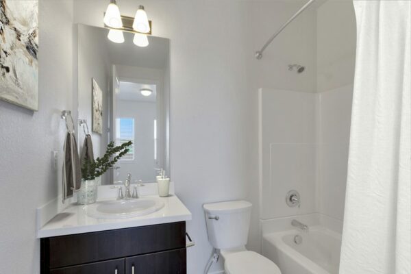 Rendering of a full bathroom with dark wood cabinets, white countertops.