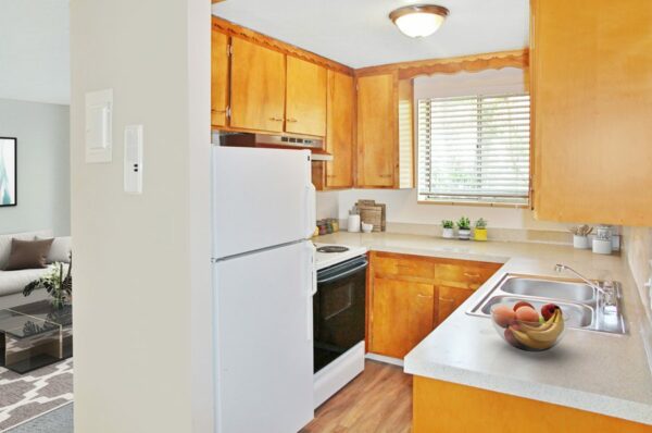 Rendering of a kitchen with wood cabinets, gray countertops, a white fridge, and a window.