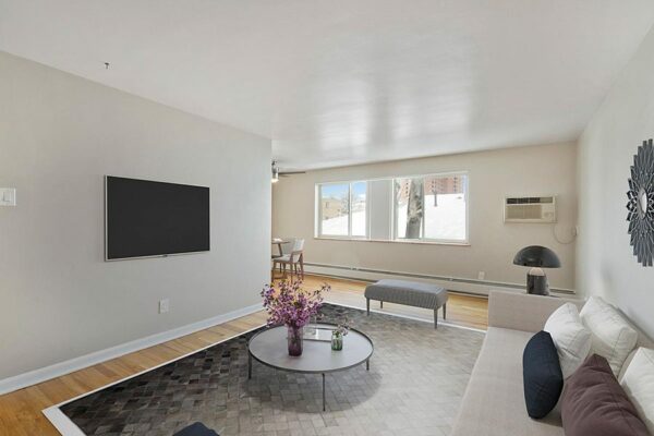 Living room with wood floor and tile, modern plush furniture, wall mounted TV, and large window.
