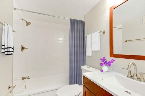 Bathroom with wood cabinet, white counter, framed mirror, and tiled shower tub.