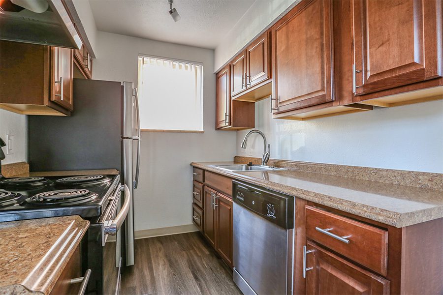 Kitchen with wood floor and cabinets, stone counters, and stainless steel appliances.