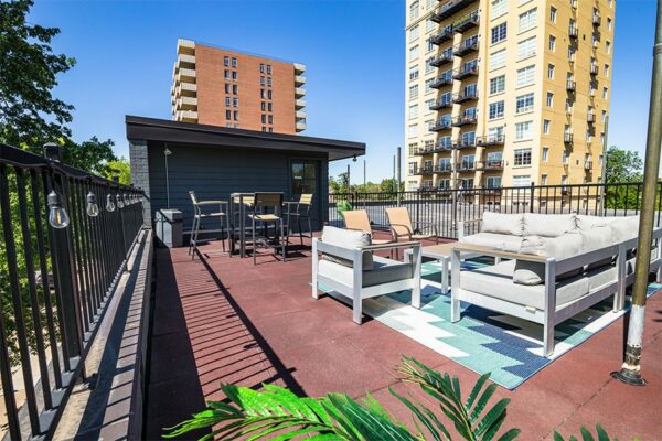 Rooftop patio with plush outdoor furniture, railings with string lights, and large plants.