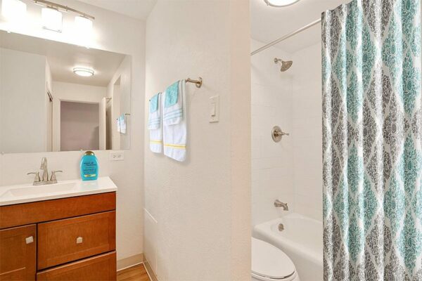 Bathroom with wood cabinet, white counter, large mirror, and tiled shower/tub.