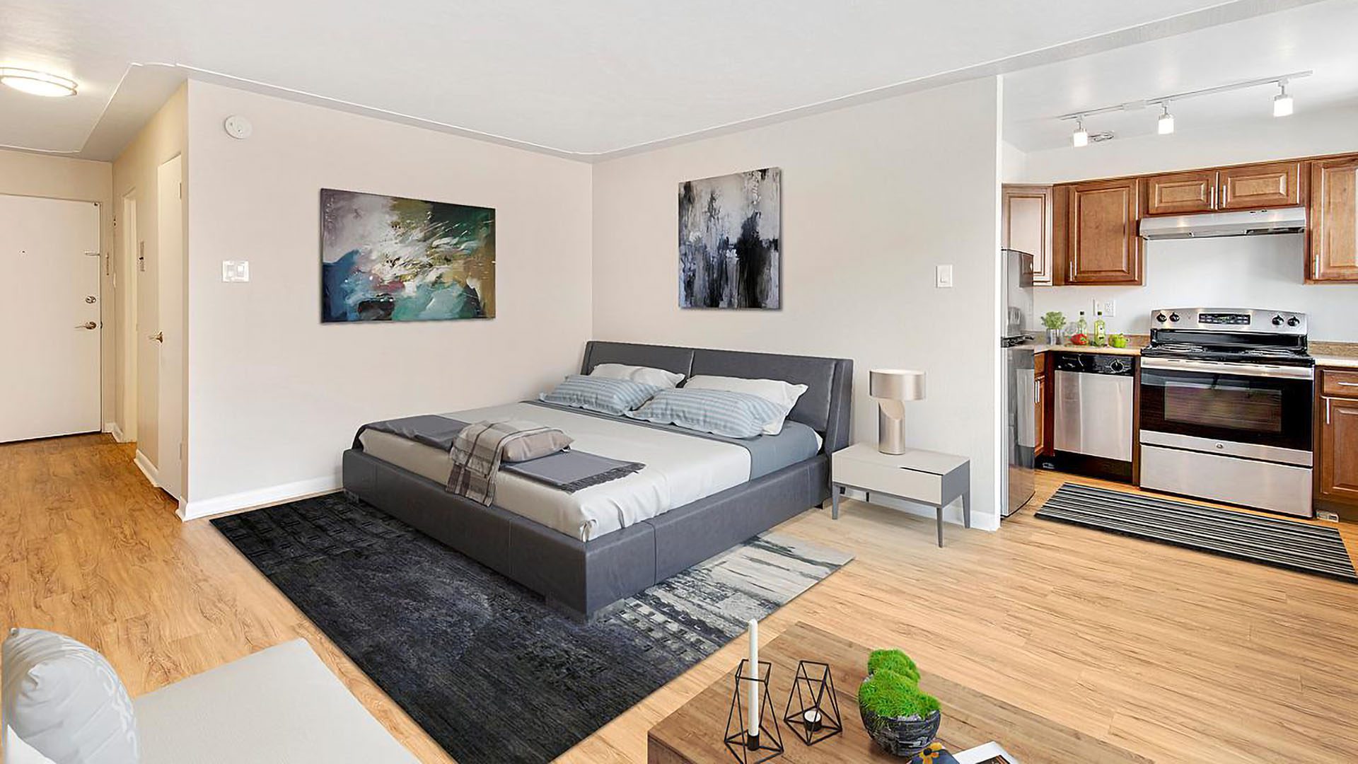 Studio living area with wood floor, plush bed, modern furnishings, and door to kitchen.