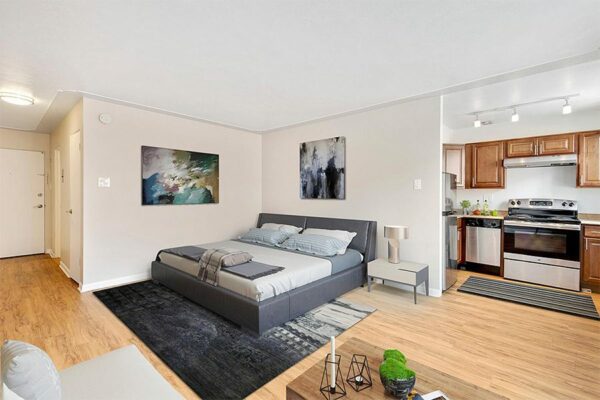 Studio living area with wood floor, plush bed, modern furnishings, and door to kitchen.