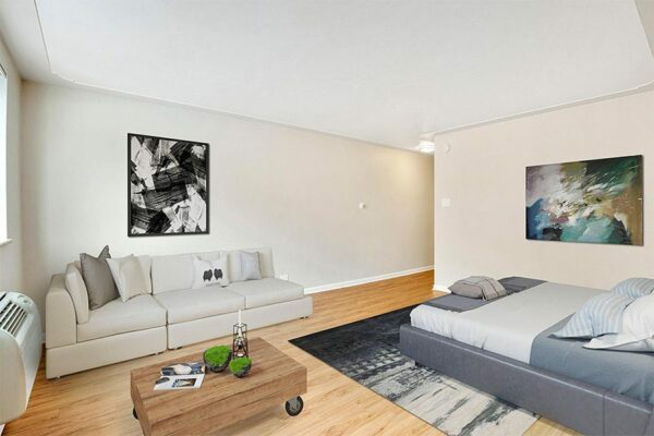 Studio living space with wood floor, plush couch and bed, wood coffee table, and large artwork.