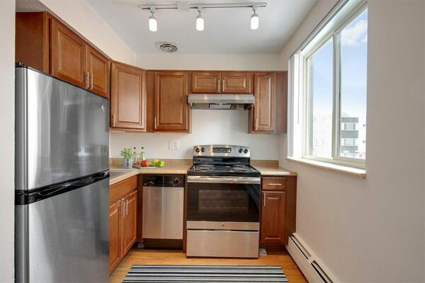 Kitchen with wood floor and cabinets, stone counters, stainless steel appliances, and large window.