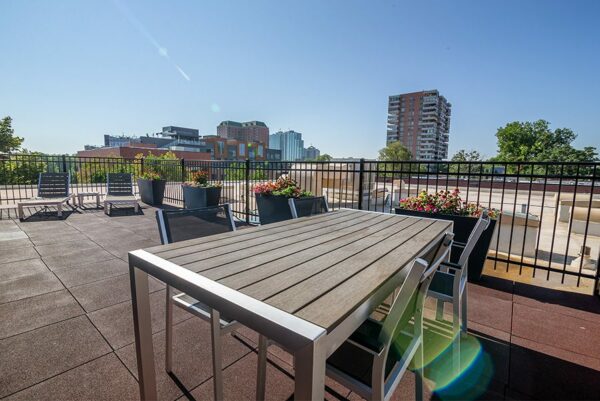 Rooftop patio with dining tables, lounge chairs, and metal railing overlooking Denver.