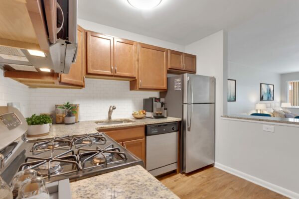 Kitchen with wood floor and cabinets, stone counters, stainless steel appliances, and tiled backsplash.