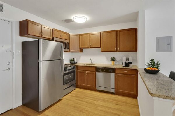 Living room with wood floors, stainless steel appliances, and dark wood cabinets.