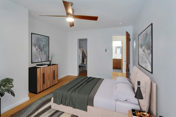 Bedroom with a carpet over wood floors, a ceiling fan, and white walls.