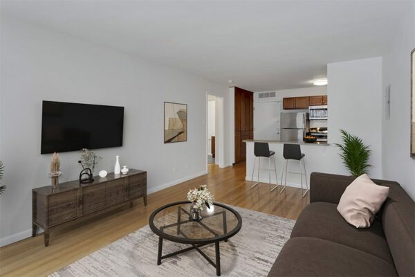 Living room with carpet over wood floors, white walls, and a view into the kitchen.