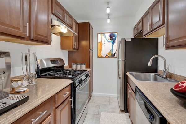 Apartment kitchen with wood floor and cabinets, stone counters, and stainless steel appliances.