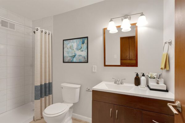 Bathroom with wood cabinets, framed mirror, and tiled shower.