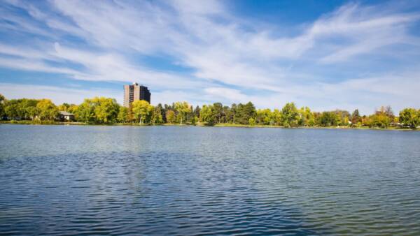 A lake surrounded by trees with a few buildings in the background.